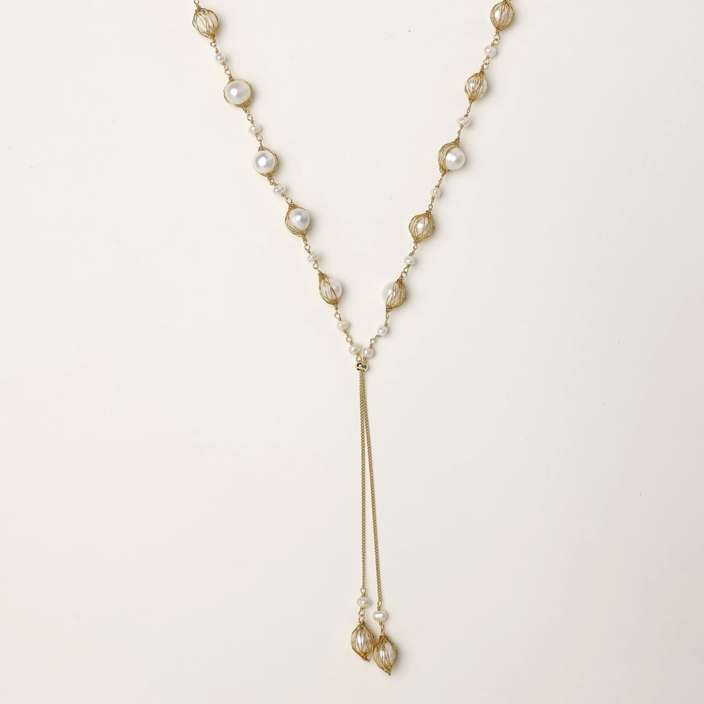 Long gold-plated lariat necklace with wire-wrapped freshwater pearls and chain tassel detail on cream background.