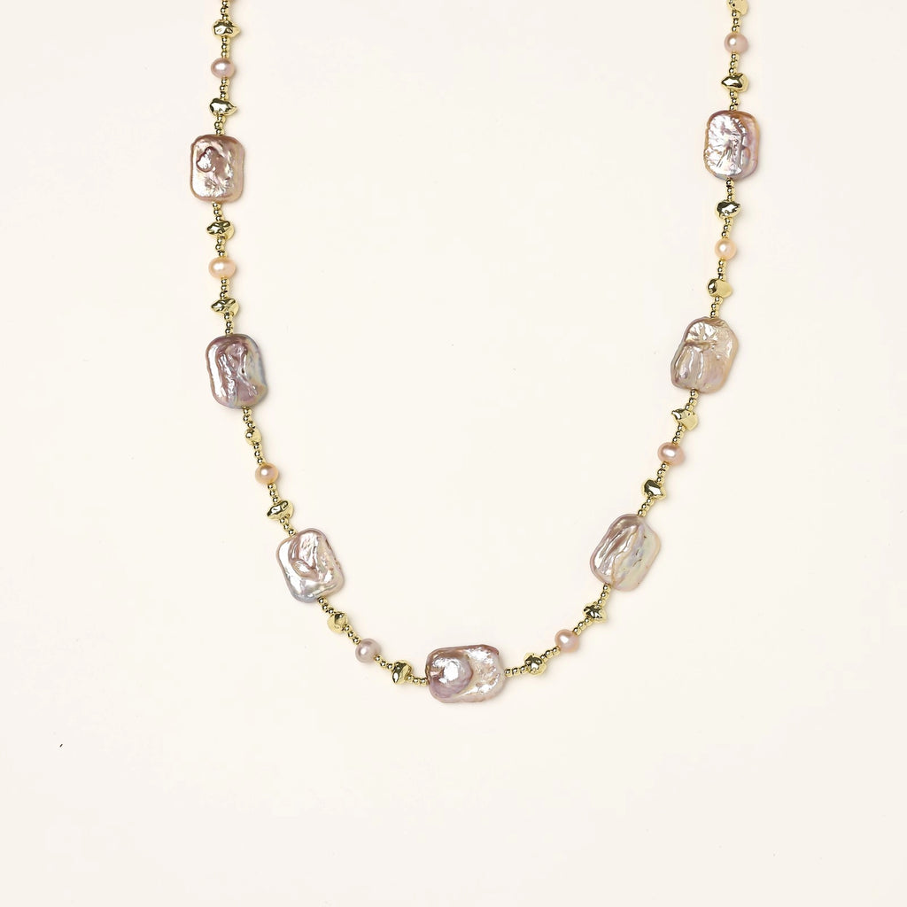 Long gold-plated necklace with iridescent baroque pearls and round freshwater pearls on cream background