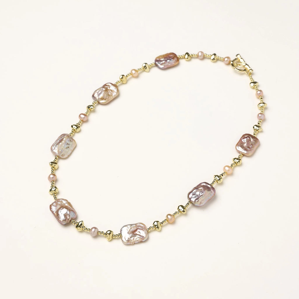 Long gold-plated necklace with iridescent baroque pearls and round freshwater pearls on cream background
