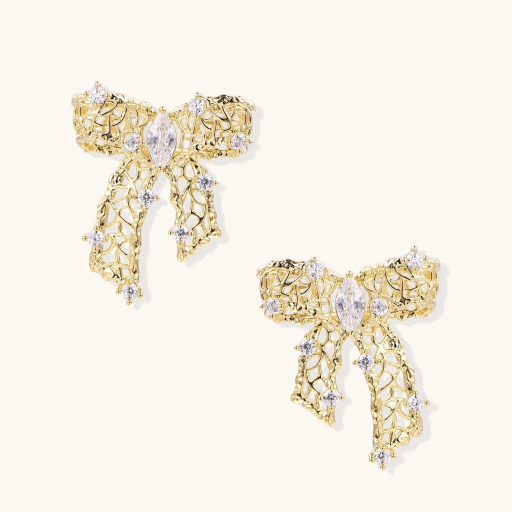 Gold and silver bow-shaped earrings with intricate lattice pattern and clear zirconia stones on neutral background.
