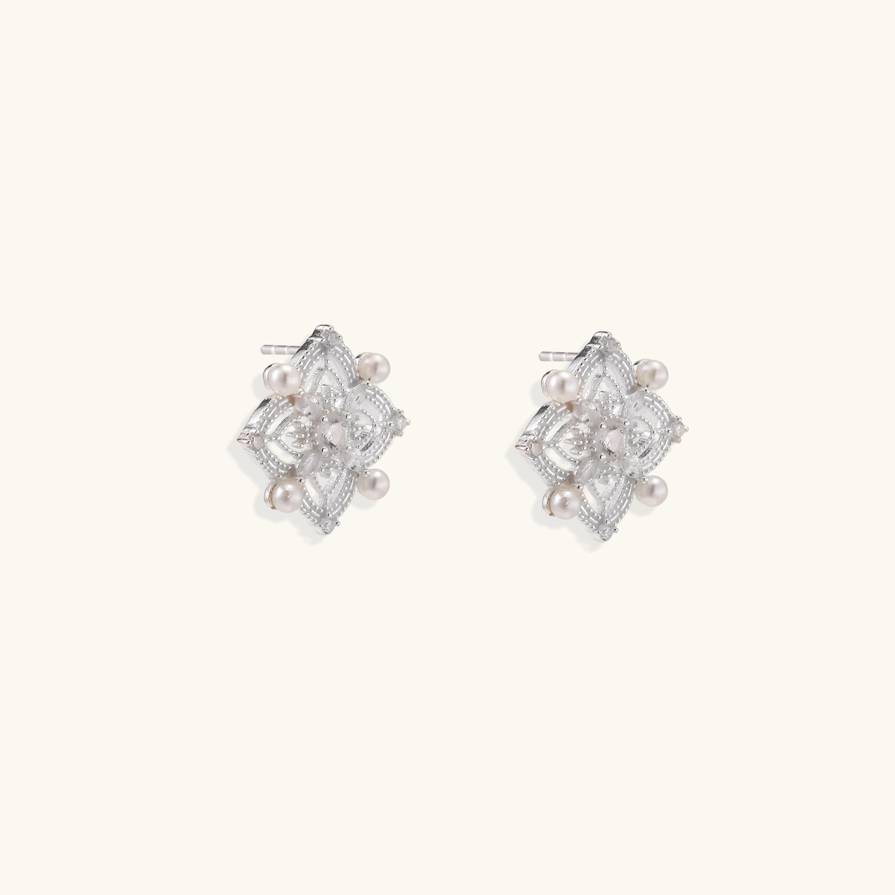 Detailed view of sterling silver stud earrings with geometric filigree design and small freshwater pearls on white background.
