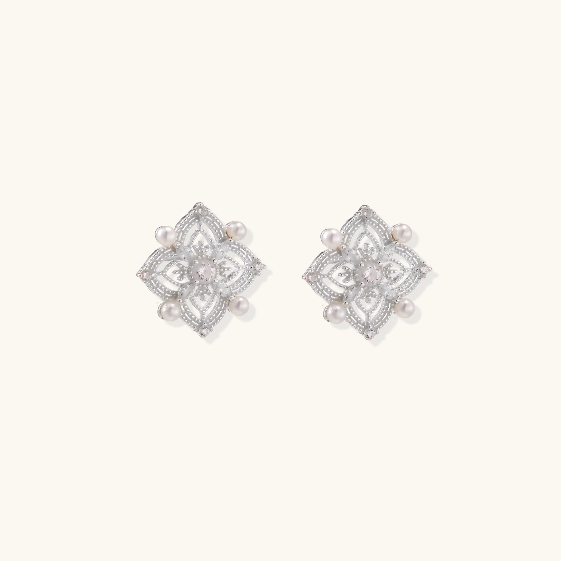 Detailed view of sterling silver stud earrings with geometric filigree design and small freshwater pearls on white background.