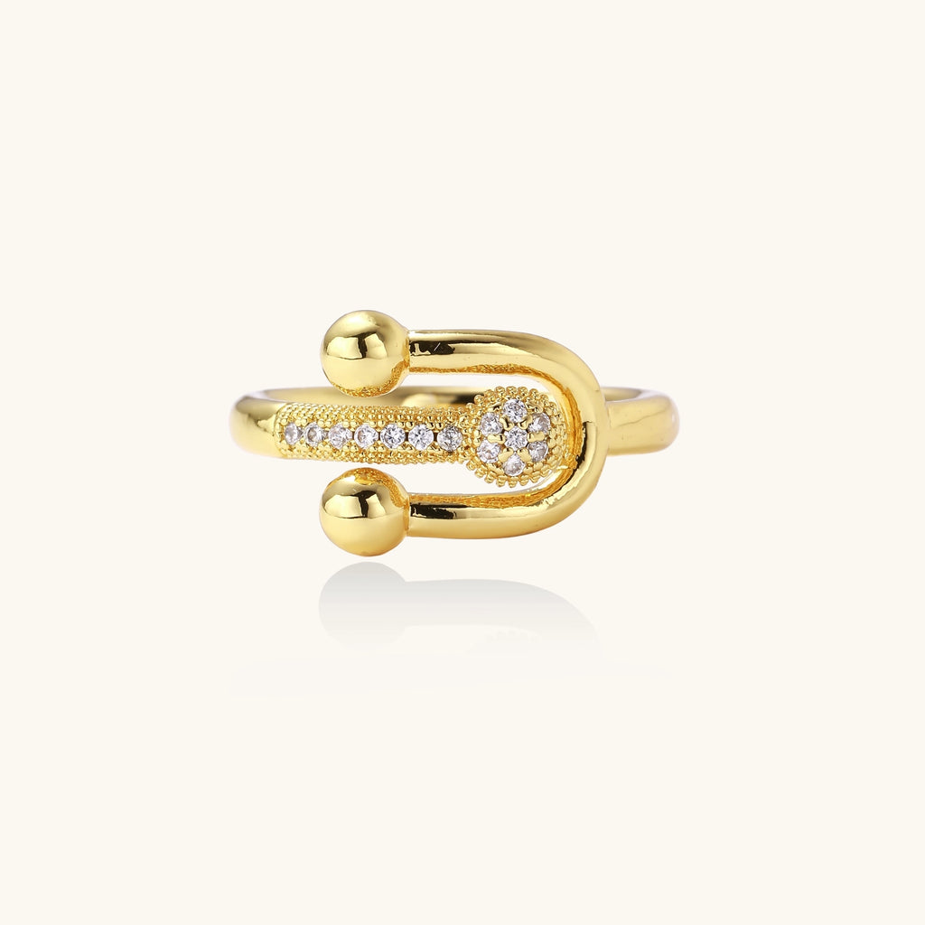 Modern gold-plated adjustable ring with safety pin design and sparkling cubic zirconia accents on white background