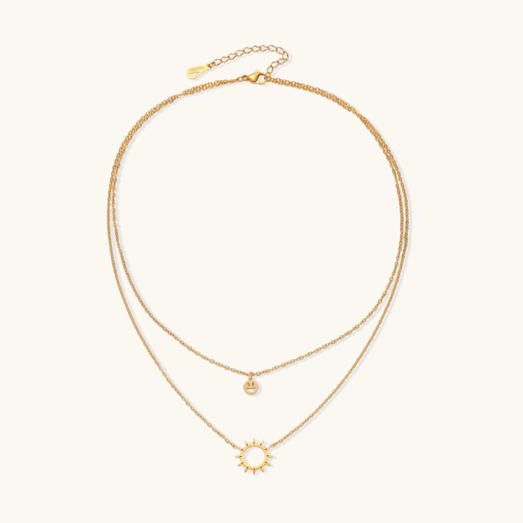 Delicate gold-plated layered necklace with smiley face and sun pendants on white background, showing adjustable chain.