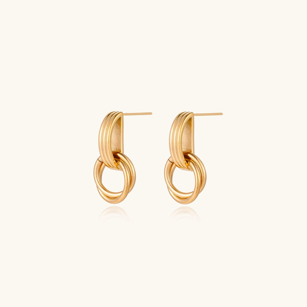 Geometric gold earrings with ribbed linear top section and circular drop elements on white background.