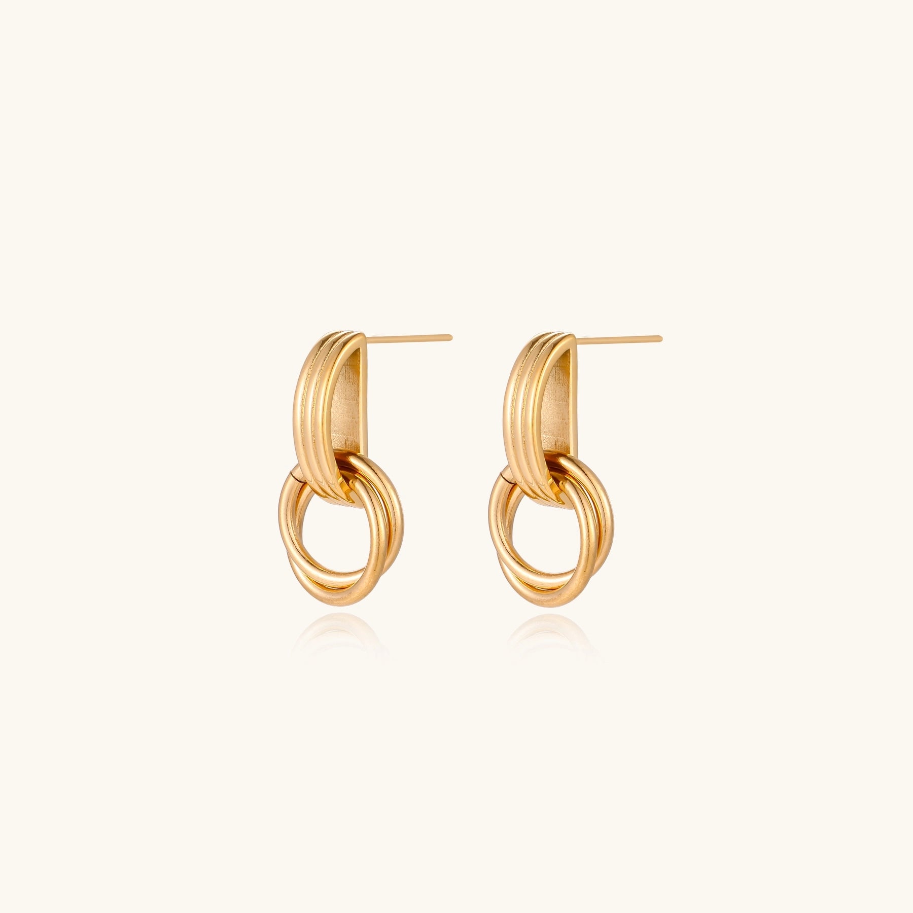Geometric gold earrings with ribbed linear top section and circular drop elements on white background.
